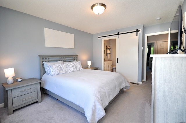 bedroom with a barn door, light carpet, baseboards, and connected bathroom
