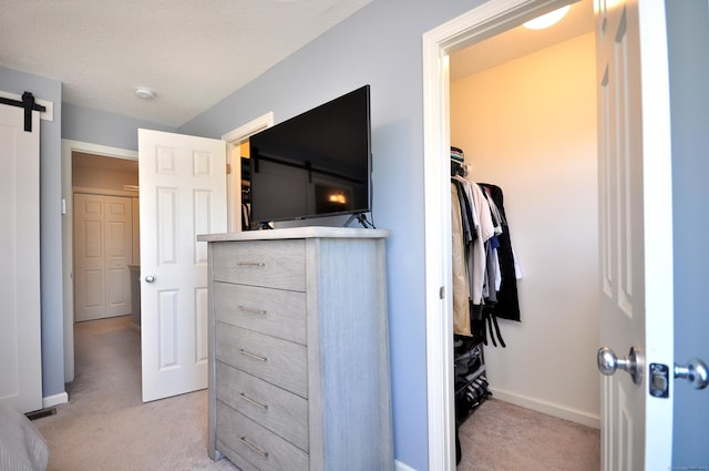 bedroom featuring light colored carpet, a barn door, and baseboards