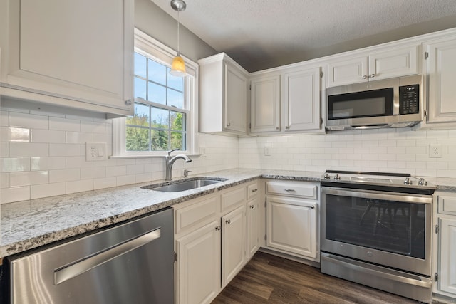 kitchen with light stone countertops, pendant lighting, dark wood-style flooring, a sink, and appliances with stainless steel finishes