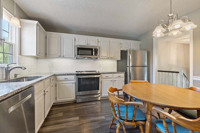 kitchen with a sink, a chandelier, stainless steel appliances, white cabinets, and dark wood-style floors