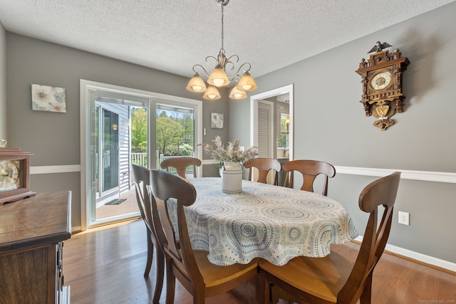 dining space featuring a chandelier, a textured ceiling, baseboards, and wood finished floors