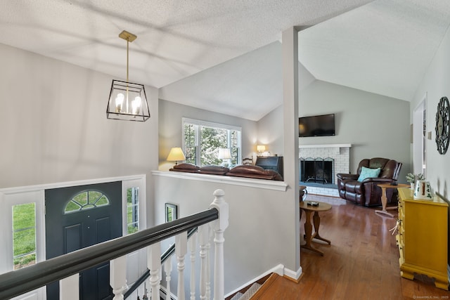 interior space featuring an inviting chandelier, wood finished floors, a brick fireplace, baseboards, and vaulted ceiling