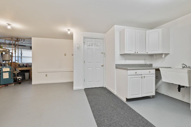 kitchen with concrete floors, a sink, a heating unit, white cabinets, and light countertops