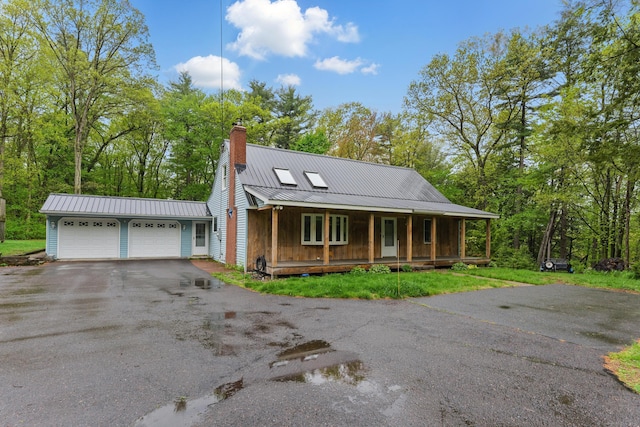 view of front of home featuring covered porch, driveway, a garage, a chimney, and metal roof