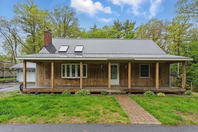 farmhouse-style home with a porch, a front lawn, a chimney, and metal roof