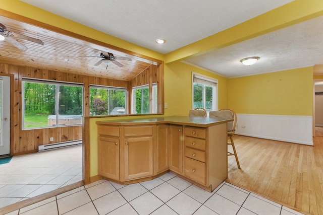 kitchen featuring a baseboard heating unit, ceiling fan, a breakfast bar, a wainscoted wall, and light tile patterned flooring