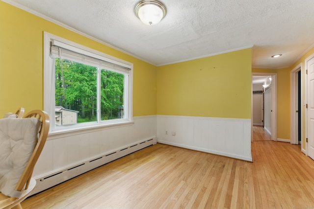 unfurnished room with a baseboard heating unit, ornamental molding, light wood finished floors, a textured ceiling, and wainscoting