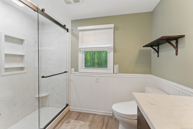 bathroom featuring wood finished floors, a stall shower, toilet, a wainscoted wall, and vanity