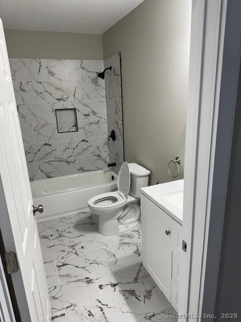 bathroom with toilet, vanity, shower / tub combination, and marble look tiles