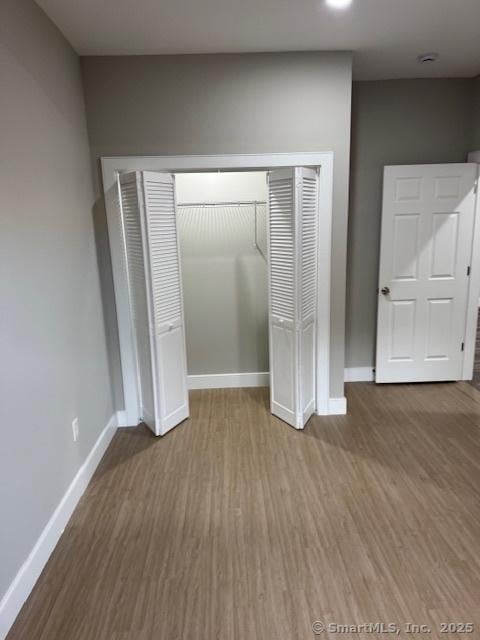 unfurnished bedroom with wood finished floors, baseboards, and a closet