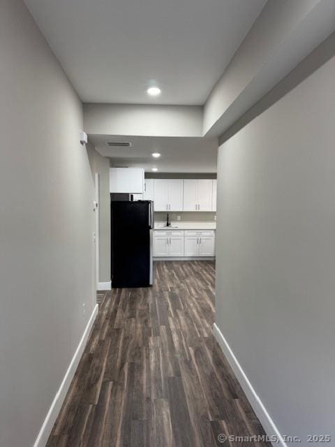 corridor with dark wood-style floors, baseboards, a sink, and recessed lighting