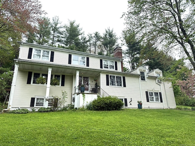 view of front facade featuring a front lawn, covered porch, and a chimney