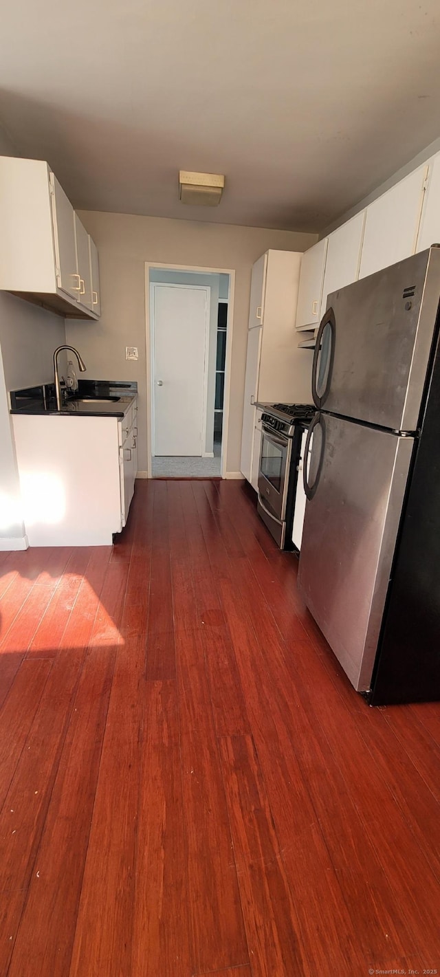 kitchen featuring baseboards, dark wood-type flooring, white cabinets, a sink, and appliances with stainless steel finishes