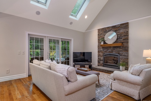 living area with high vaulted ceiling, a skylight, a fireplace, light wood finished floors, and baseboards