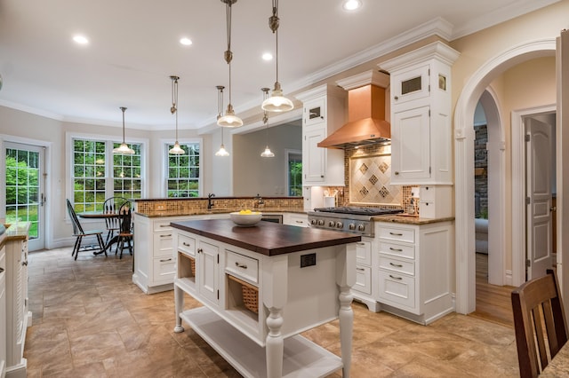 kitchen with butcher block countertops, a peninsula, wall chimney range hood, open shelves, and tasteful backsplash