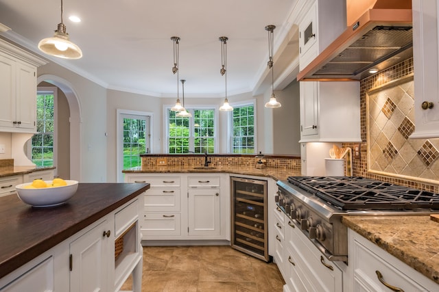 kitchen featuring wine cooler, wall chimney exhaust hood, stainless steel gas stovetop, butcher block counters, and healthy amount of natural light