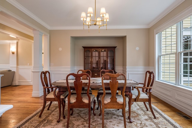 dining room featuring plenty of natural light, light wood-style floors, ornamental molding, a chandelier, and a wainscoted wall