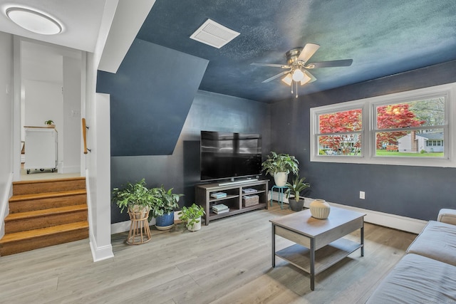 living area with visible vents, wood finished floors, baseboards, ceiling fan, and stairway