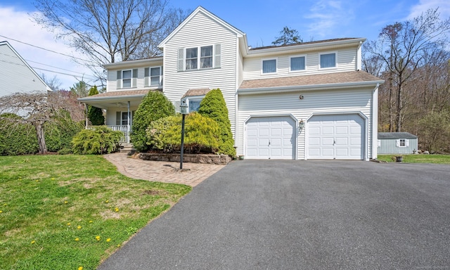 traditional-style home featuring asphalt driveway, an attached garage, a front yard, and a porch