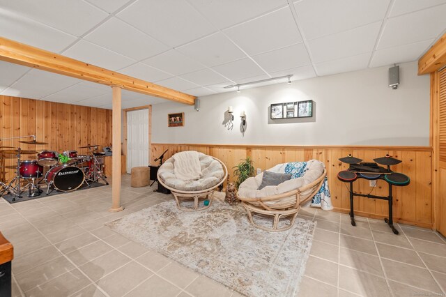 sitting room with tile patterned floors, wooden walls, a paneled ceiling, and wainscoting