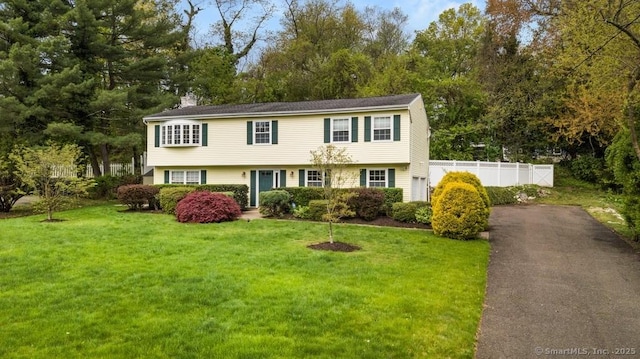 colonial-style house featuring aphalt driveway, fence, a chimney, and a front yard