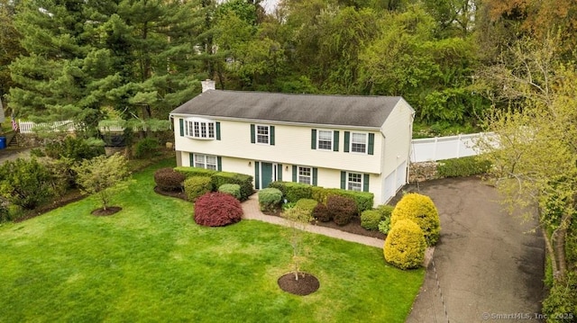 colonial-style house featuring a chimney, aphalt driveway, a front lawn, and fence
