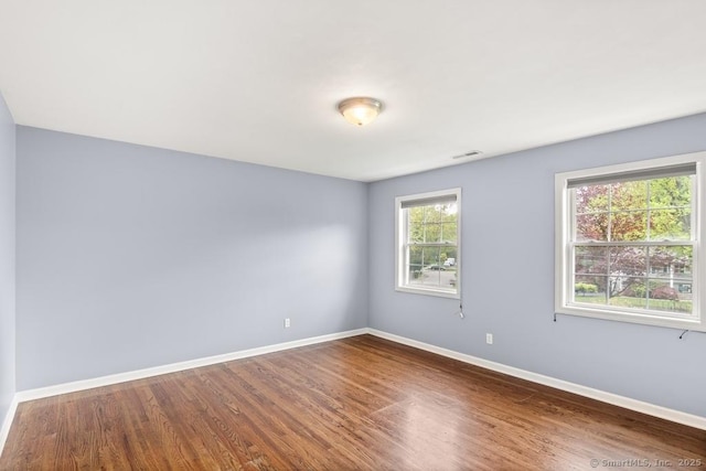 unfurnished room with baseboards, visible vents, and wood finished floors