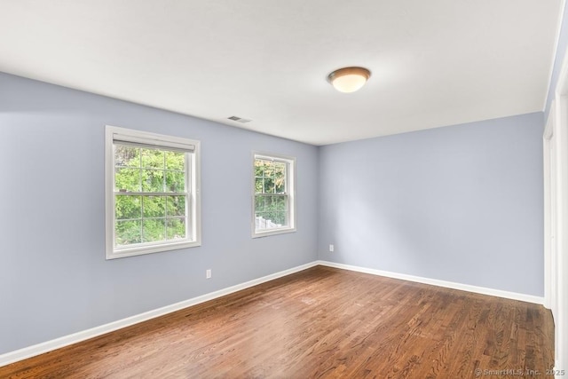 spare room with baseboards, visible vents, and wood finished floors