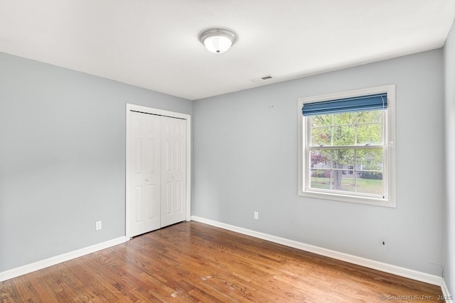 unfurnished bedroom featuring baseboards, a closet, visible vents, and wood finished floors