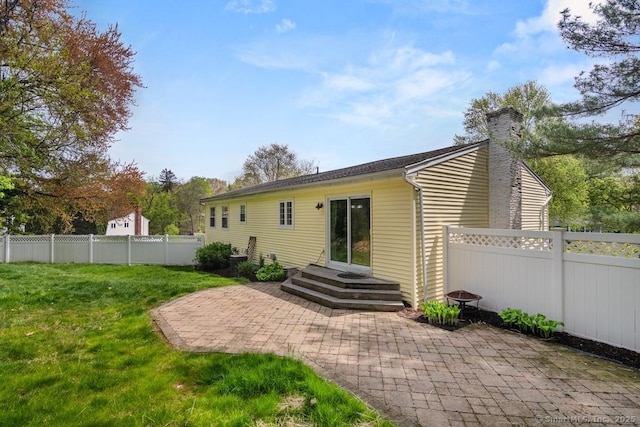 rear view of house with a lawn, a chimney, a patio, and a fenced backyard