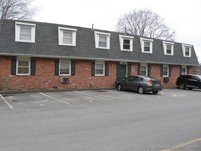 exterior space with uncovered parking, a shingled roof, brick siding, and mansard roof