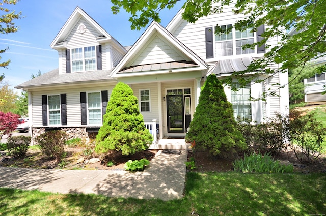 view of front facade featuring a shingled roof, a front yard, a standing seam roof, covered porch, and metal roof