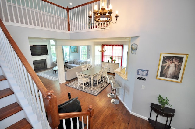 interior space featuring a high ceiling, an inviting chandelier, a glass covered fireplace, stairs, and wood finished floors