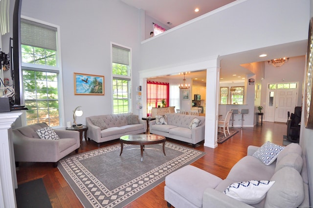 living room featuring ornate columns, a chandelier, wood finished floors, and a towering ceiling