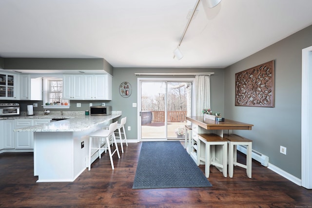 kitchen featuring a peninsula, a breakfast bar area, rail lighting, stainless steel microwave, and a baseboard radiator
