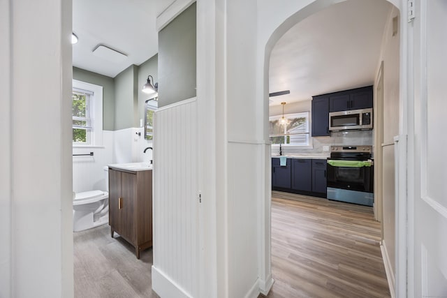 hall featuring a sink, light wood-style flooring, arched walkways, and a wainscoted wall
