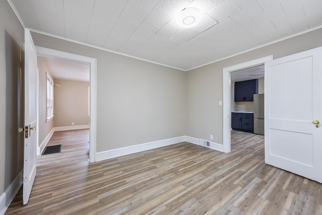 empty room with light wood-style floors, visible vents, baseboards, and ornamental molding