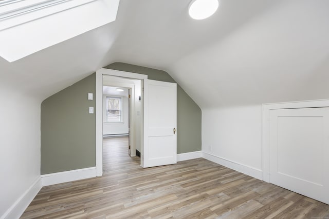bonus room featuring light wood-type flooring, baseboards, baseboard heating, and vaulted ceiling with skylight