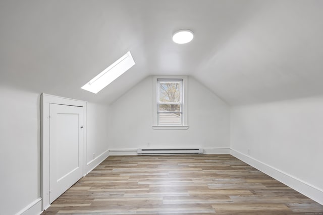 additional living space with light wood finished floors, baseboards, a baseboard radiator, and vaulted ceiling with skylight