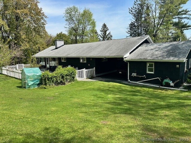 rear view of property with a chimney, fence, and a lawn