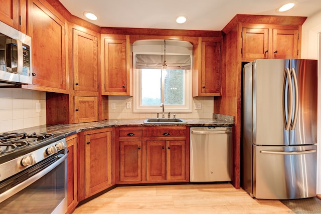 kitchen with appliances with stainless steel finishes, a sink, brown cabinets, tasteful backsplash, and recessed lighting