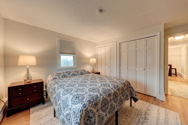 bedroom with multiple closets, light wood-style floors, and baseboard heating