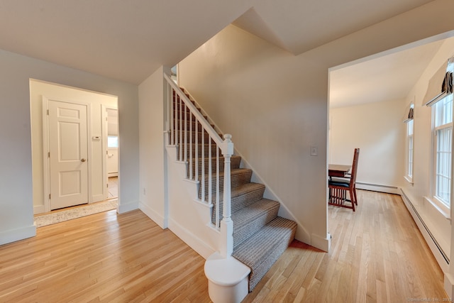 staircase featuring wood finished floors, a baseboard heating unit, and baseboards
