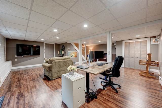 office area with baseboards, wood finished floors, and a drop ceiling