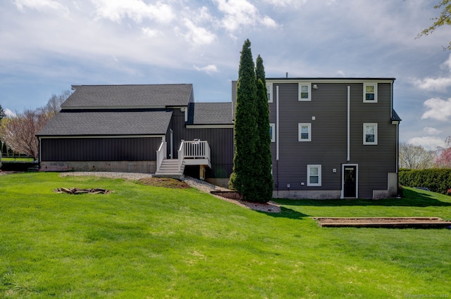 rear view of property featuring a yard, a wooden deck, and roof with shingles