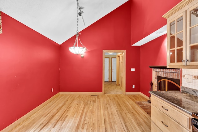 unfurnished dining area with light wood-type flooring, baseboards, high vaulted ceiling, a fireplace, and track lighting
