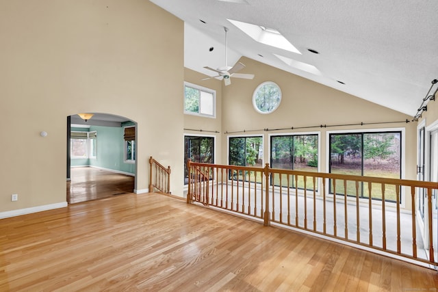 spare room featuring a skylight, high vaulted ceiling, wood finished floors, arched walkways, and ceiling fan
