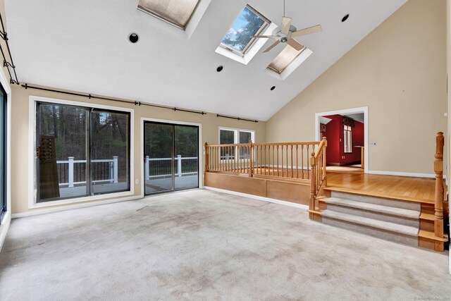 unfurnished living room with high vaulted ceiling, a skylight, stairway, baseboards, and carpet flooring
