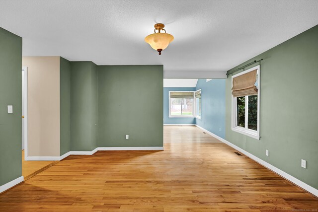 spare room with light wood-style floors, baseboards, and a textured ceiling
