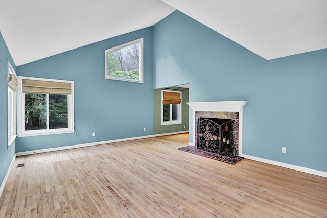 unfurnished living room with high vaulted ceiling, a tiled fireplace, wood finished floors, and plenty of natural light